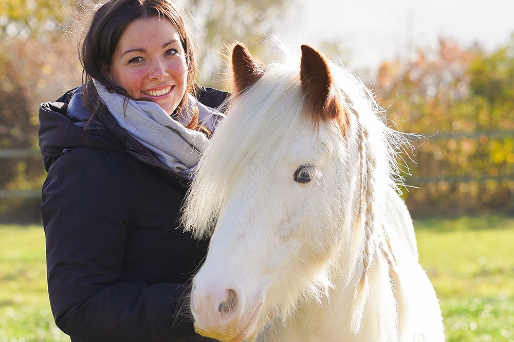 Christina Pavel mit weißem Ponny an einem sonnigen Tag