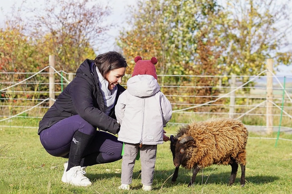 Christina Pavel und ein Kind streicheln einen kleinen Schafsbock bei sonnigem Wetter
