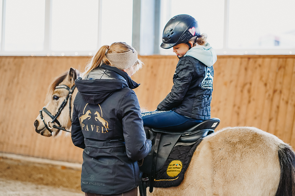Kind sitzt auf Ponny, Trainerin hilft beim Sattel