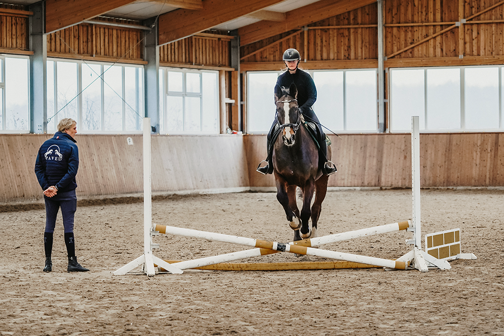 In Reithalle: Reitschülerin auf Pferd nähert sich Hindernis, Philipp Pavel beobachtet