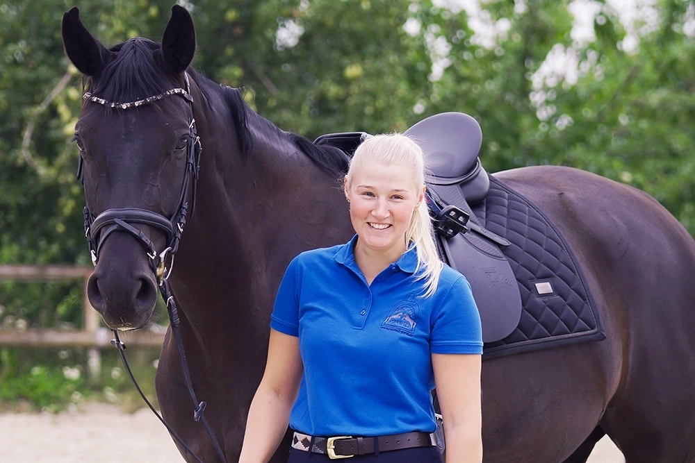 Celina steht neben schwarzbraunem Pferd, hält Zügel in Hand