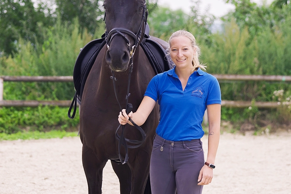 Dani steht neben braunem Pferd, hält Zügel in Hand