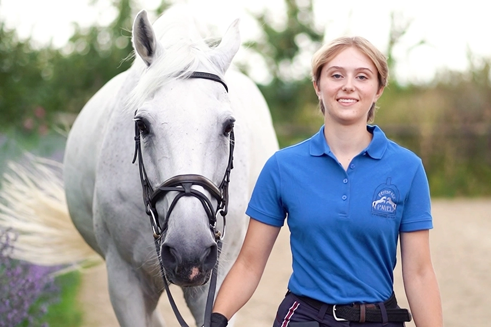 Laetitia führt weißes Pferd, hält Zügel in Hand