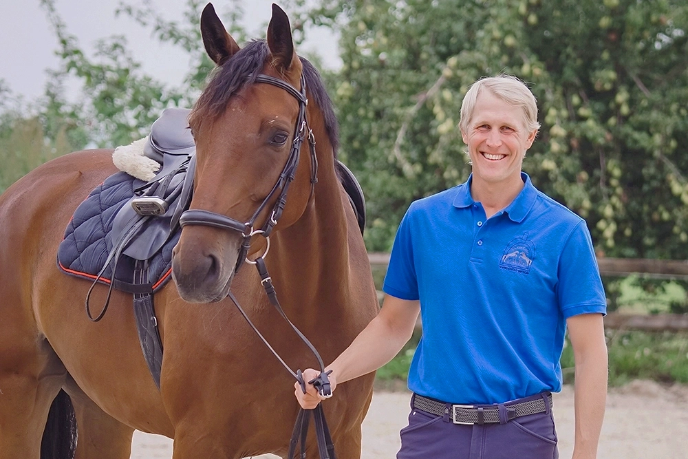 Philipp Pavel steht neben braunem Pferd, hält Zügel in Hand